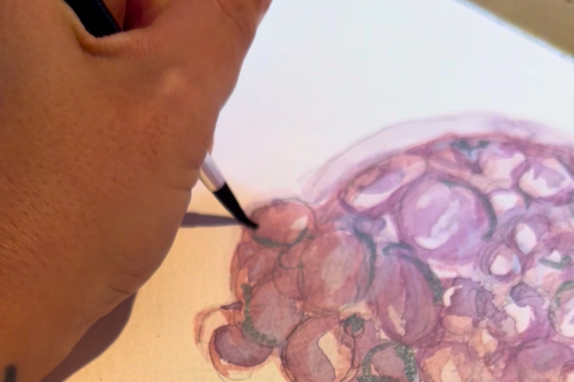 hand holding paintbrush painting a pink/purple embryo