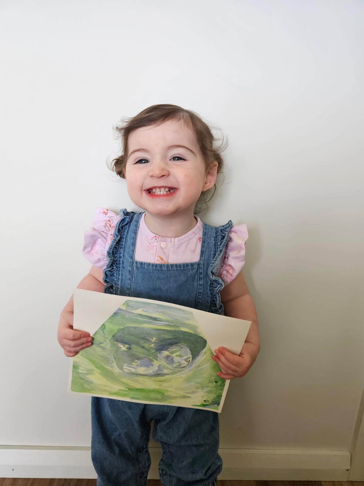 Child holding a green watercolour ultrasound painting against a white wall