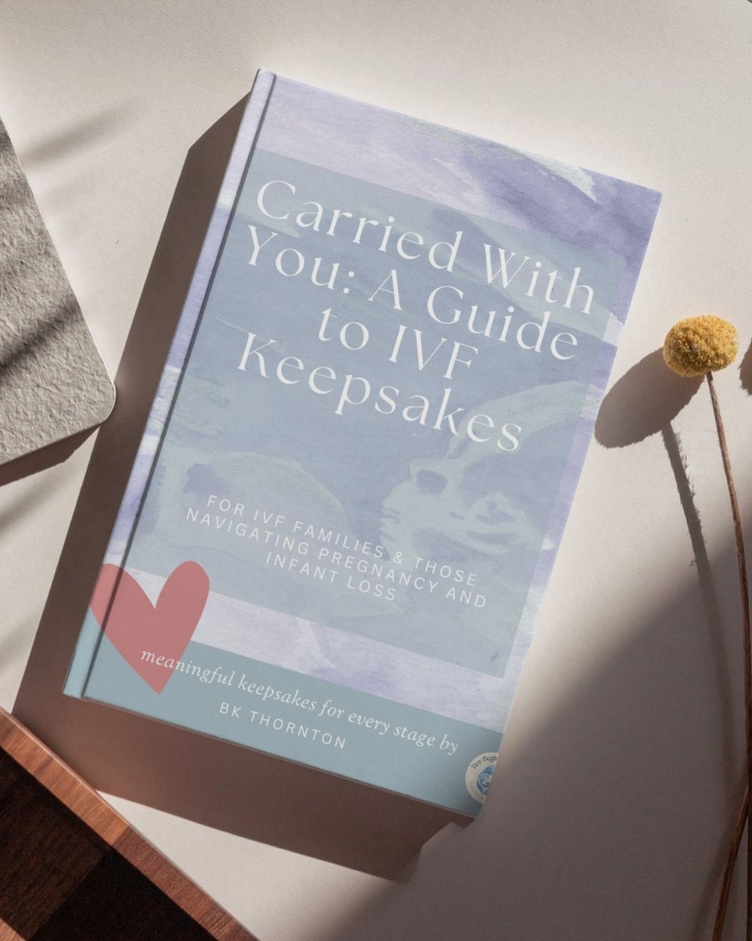 Book titled 'Carried With You: A Guide to IVF Keepsakes' on a light surface with a heart symbol.