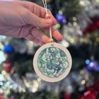 Hand holding a round decorative embryo painting with a Christmas tree in the background
