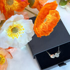 Silver necklace in a black box surrounded by orange and white flowers on a white background