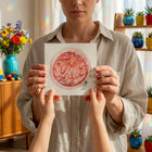 Person holding a pink watercolour embryo on it in front of their face, in a room with plants and toys.