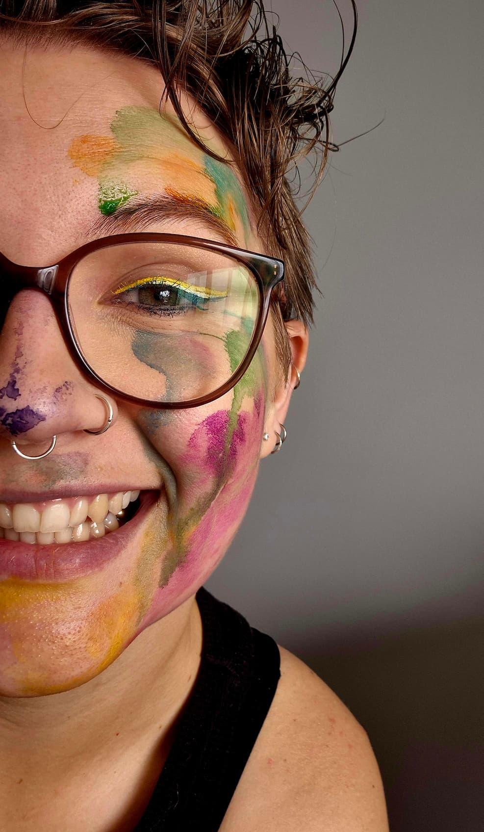 Selfie of the artist with colorful face paint and glasses against a neutral background