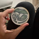 hand holding a green hand painted wooden christmas ornament of a baby ultrasound sonogram