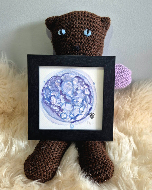 crochet bear holding framed blue and purple embryo watercolour painting