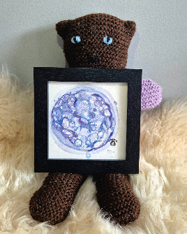 crocheted bear holding a blue watercolour blastocyst 5 day embryo painting in a black frame