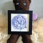 crocheted bear holding a blue watercolour blastocyst 5 day embryo painting in a black frame