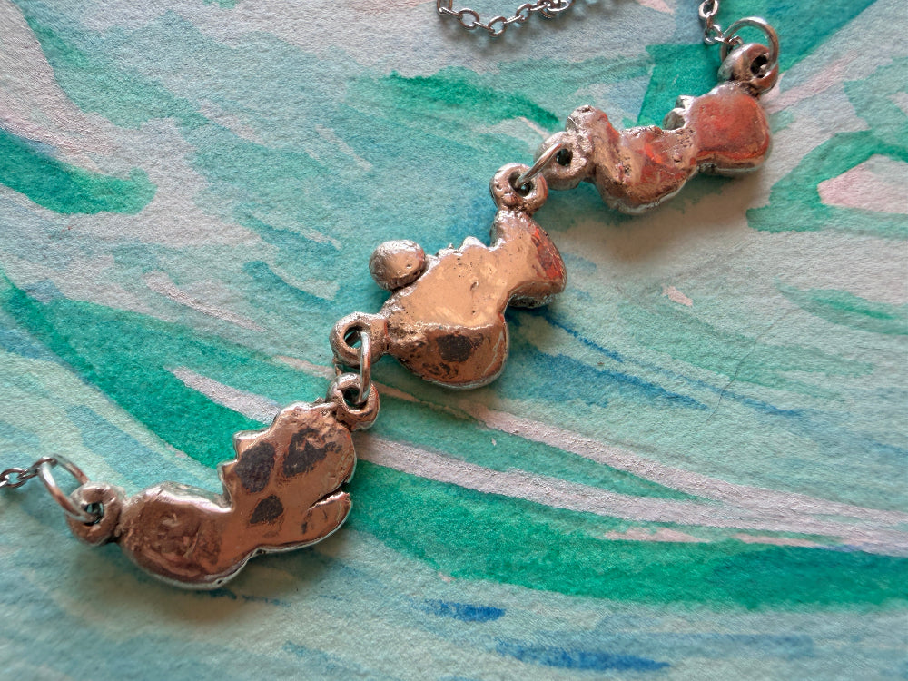 fine silver ultrasound pendant on a chain against a textured green and blue background