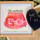 Framed artwork with a pink fetus illustration and elephants, next to a heart-shaped sign.