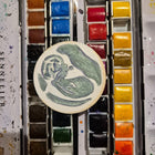 hand painted christmas ornament of a baby ultrasound placed on a watercolour palette